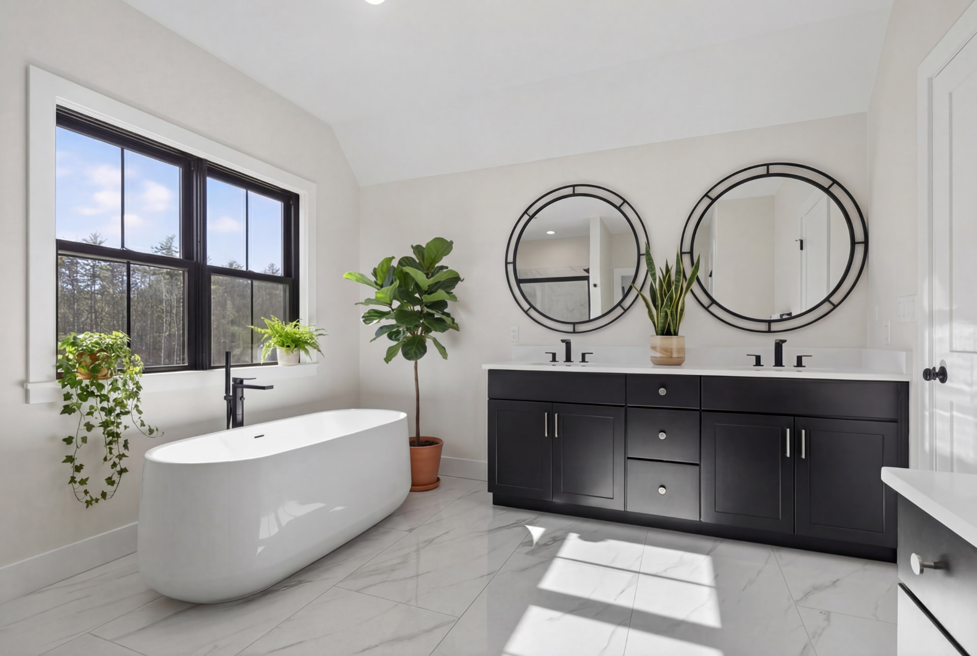 Primary bath with freestanding tub, black double vanity, and round mirrors
