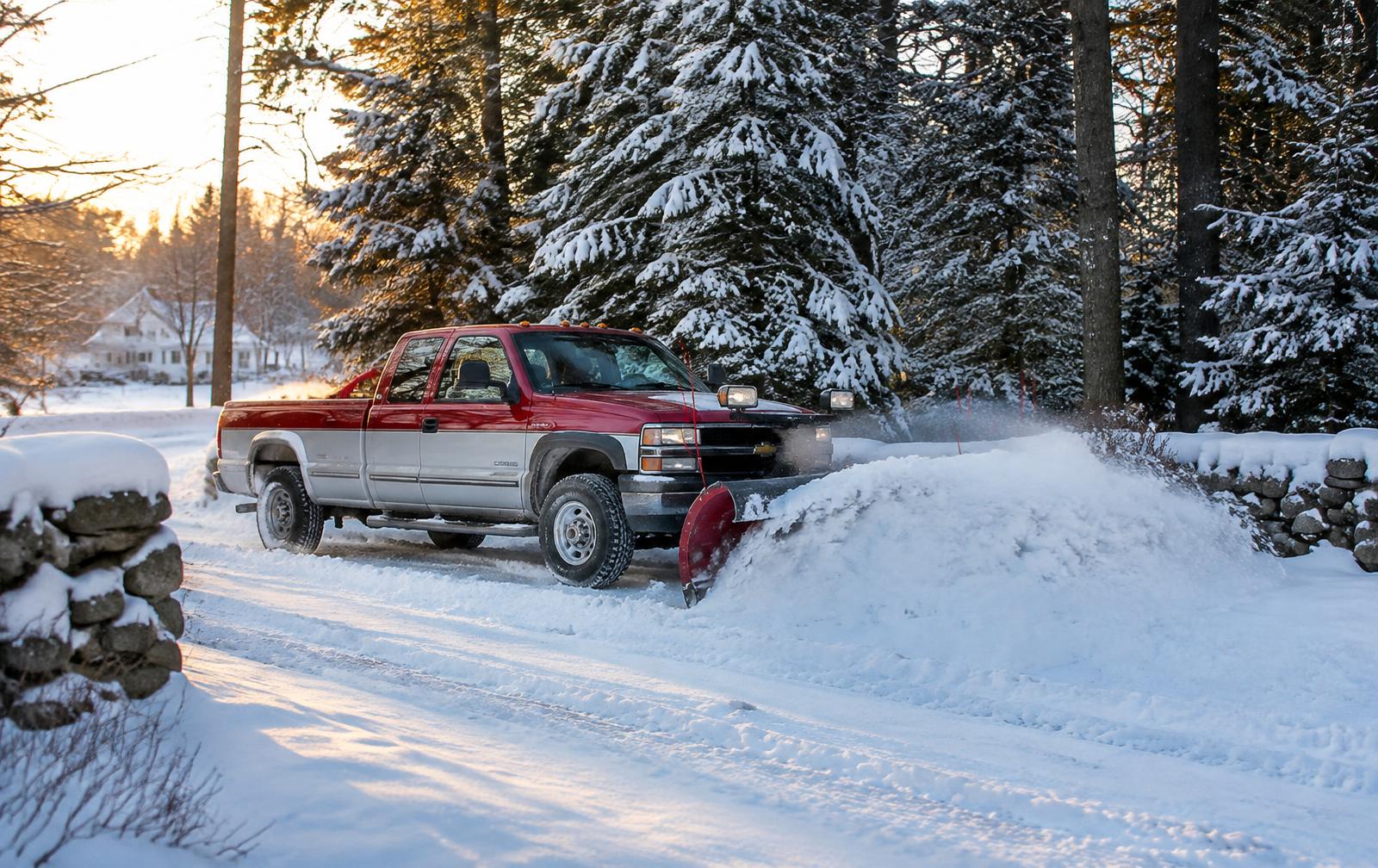 Pickup truck plowing heavy snow along a rural New Hampshire driveway lined with stone walls