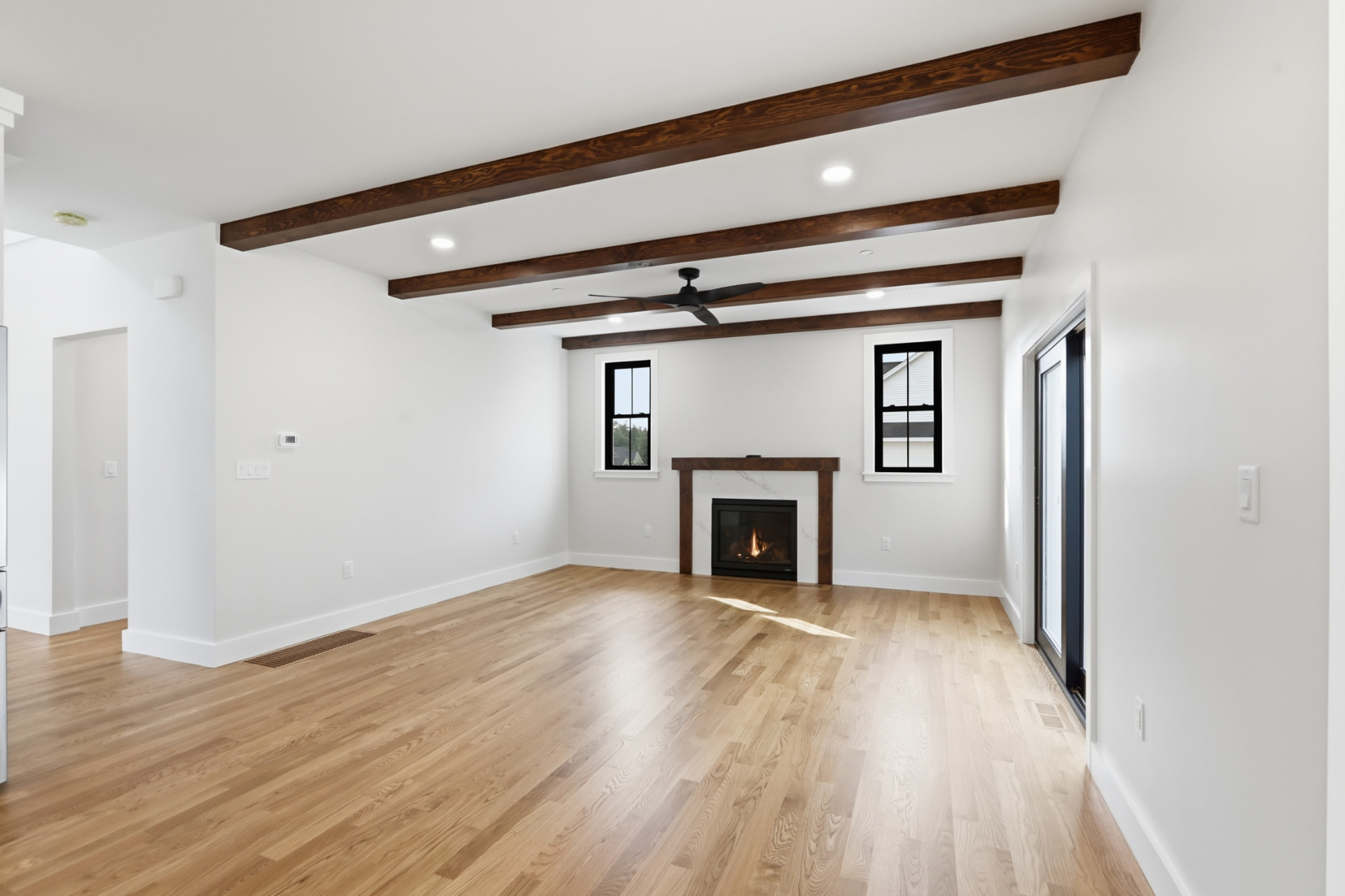 Great room with stained ceiling beams, gas fireplace, and white oak flooring